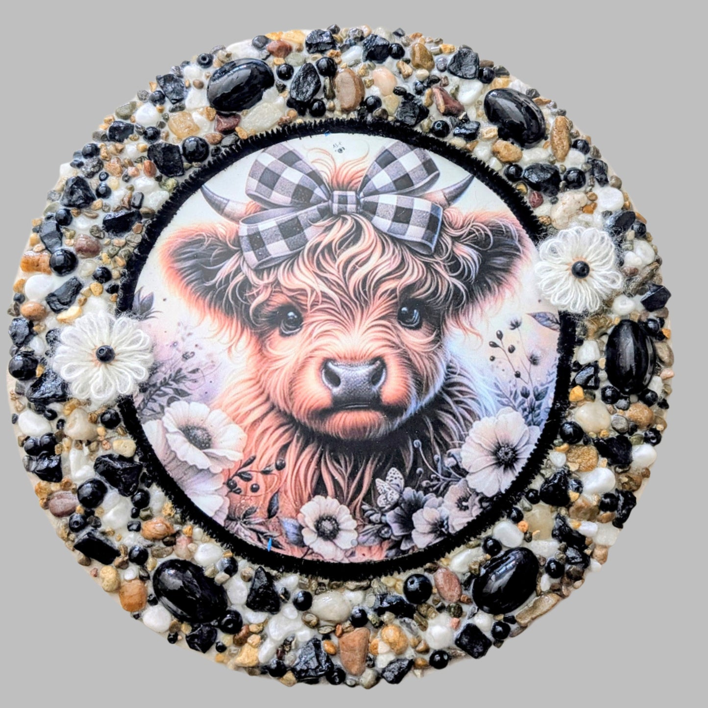 "The Tartan Heifer" is a handmade canvas featuring a print of a tartan-adorned cow decorated with white flowers, shiny stones, and earthy accents.