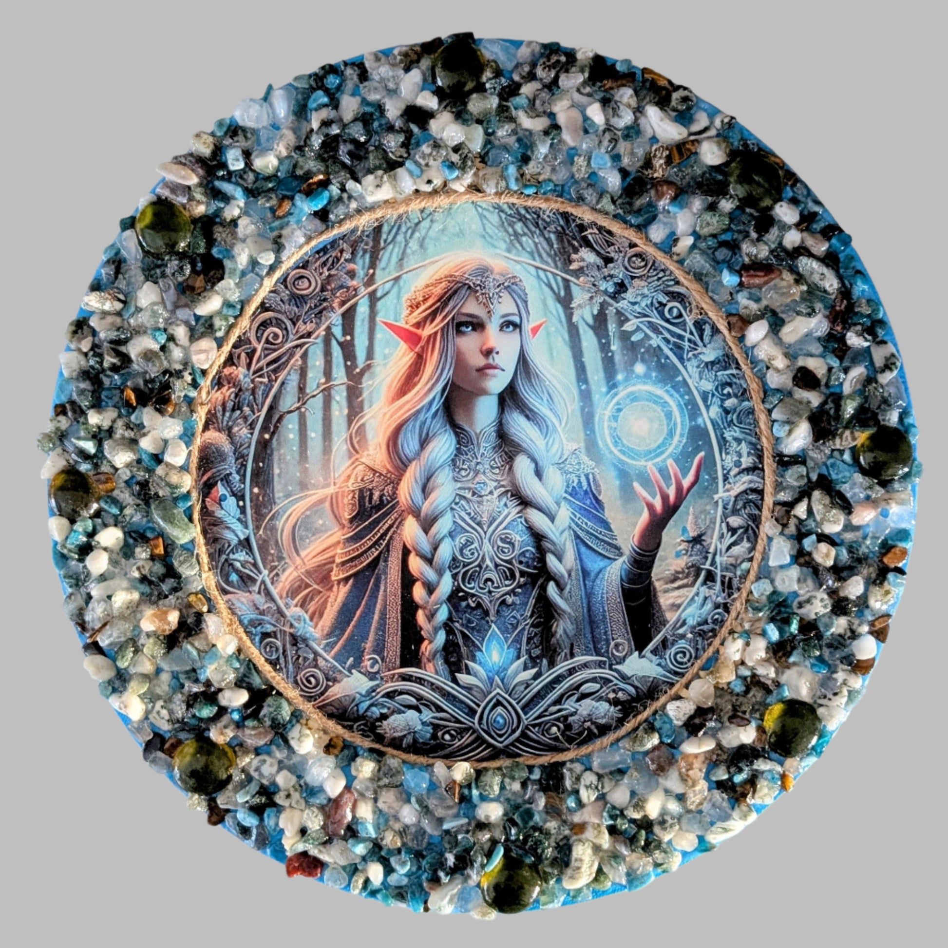 "Celestial Brilliance" is a handmade canvas featuring a print of a glowing fairy in blue and gold, decorated with vibrant and earthy stones & pebbles.