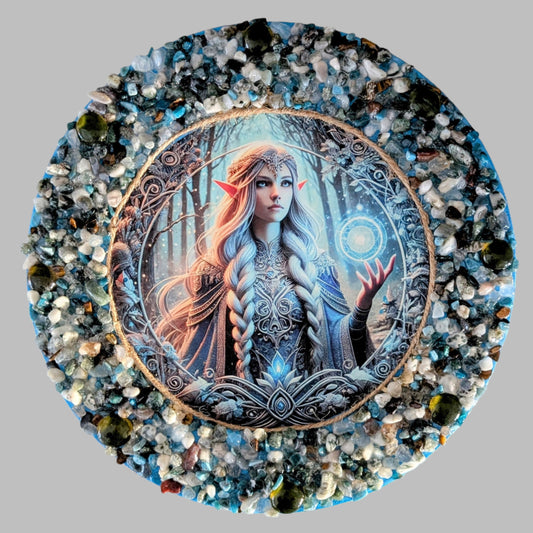 "Celestial Brilliance" is a handmade canvas featuring a print of a glowing fairy in blue and gold, decorated with vibrant and earthy stones & pebbles.