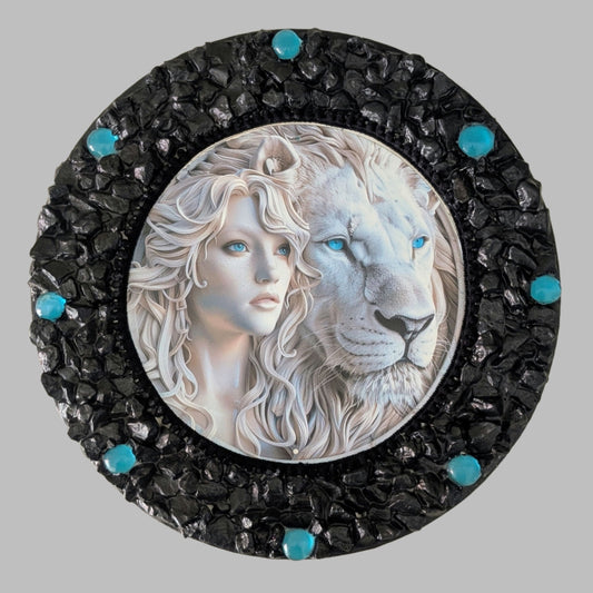"Blue Mystique" is a handmade canvas featuring a print of a white lion and woman with striking blue eyes, framed by black and bright blue stones.