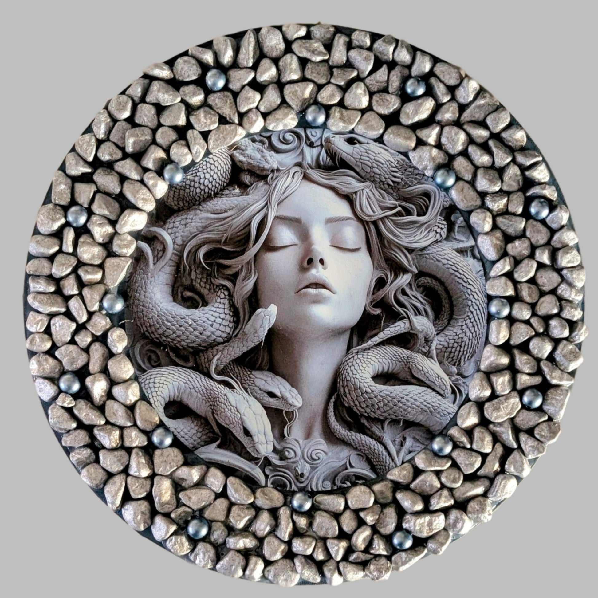 "Medusa's Embrace" is a handmade canvas featuring a print of Medusa surrounded by serpents, decorated with grey stones, and blue beads symbolising beauty and power.