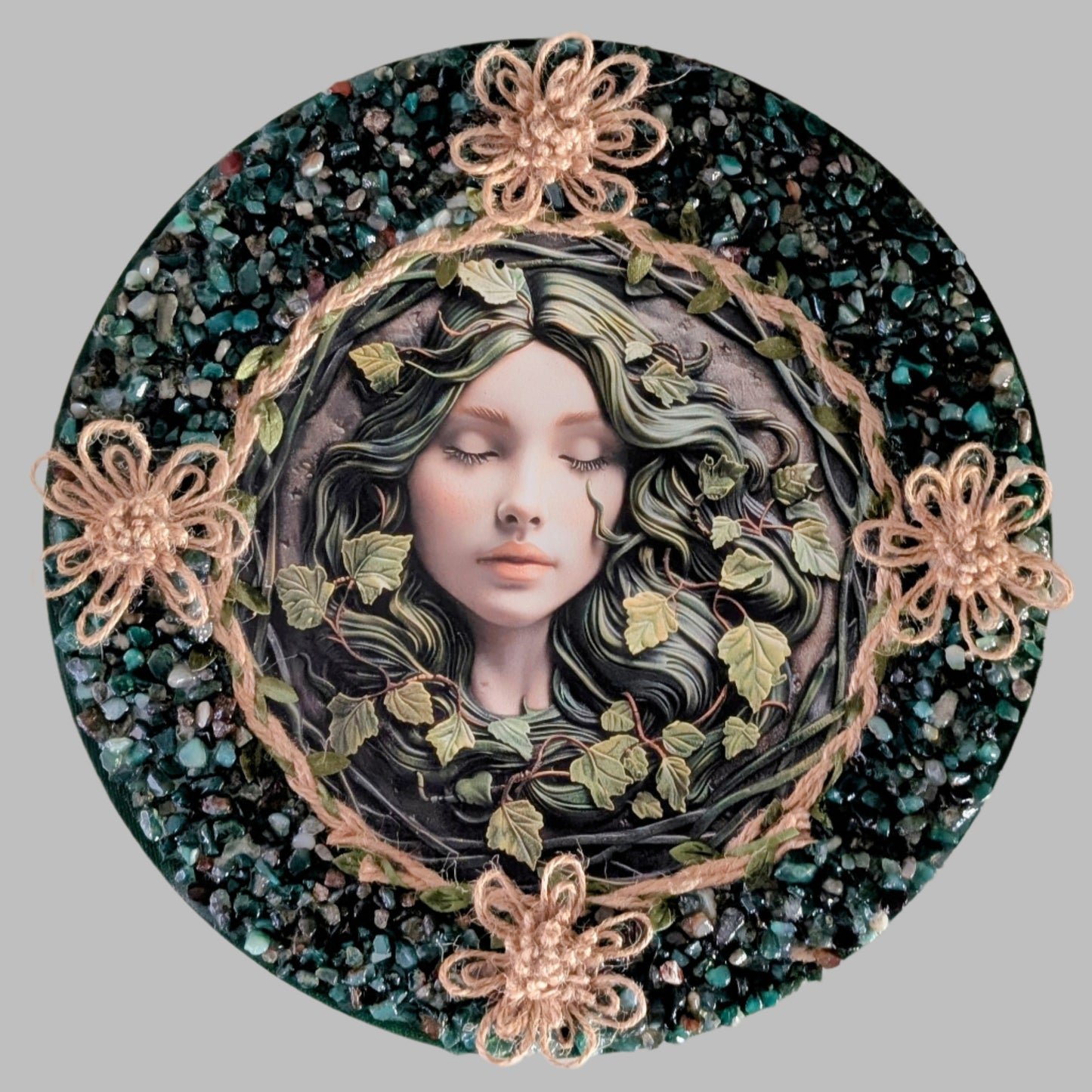 "The Sleeping Grove" is a handmade canvas featuring a print of a sleeping fairy surrounded by vines, decorated with rope flowers, and vibrant green stones.