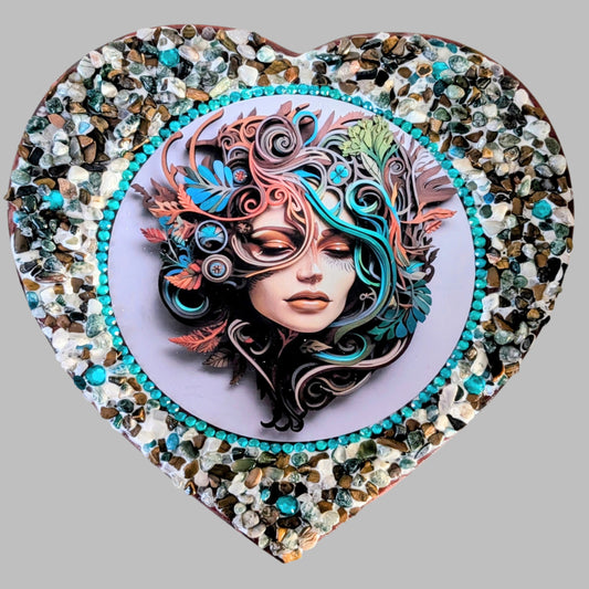 "Echoes of the Heart" is a handmade heart shaped canvas with a print of a woman surrounded by swirling blue and earthy coloured leaves, decorated with earthy coloured stones & pebbles.