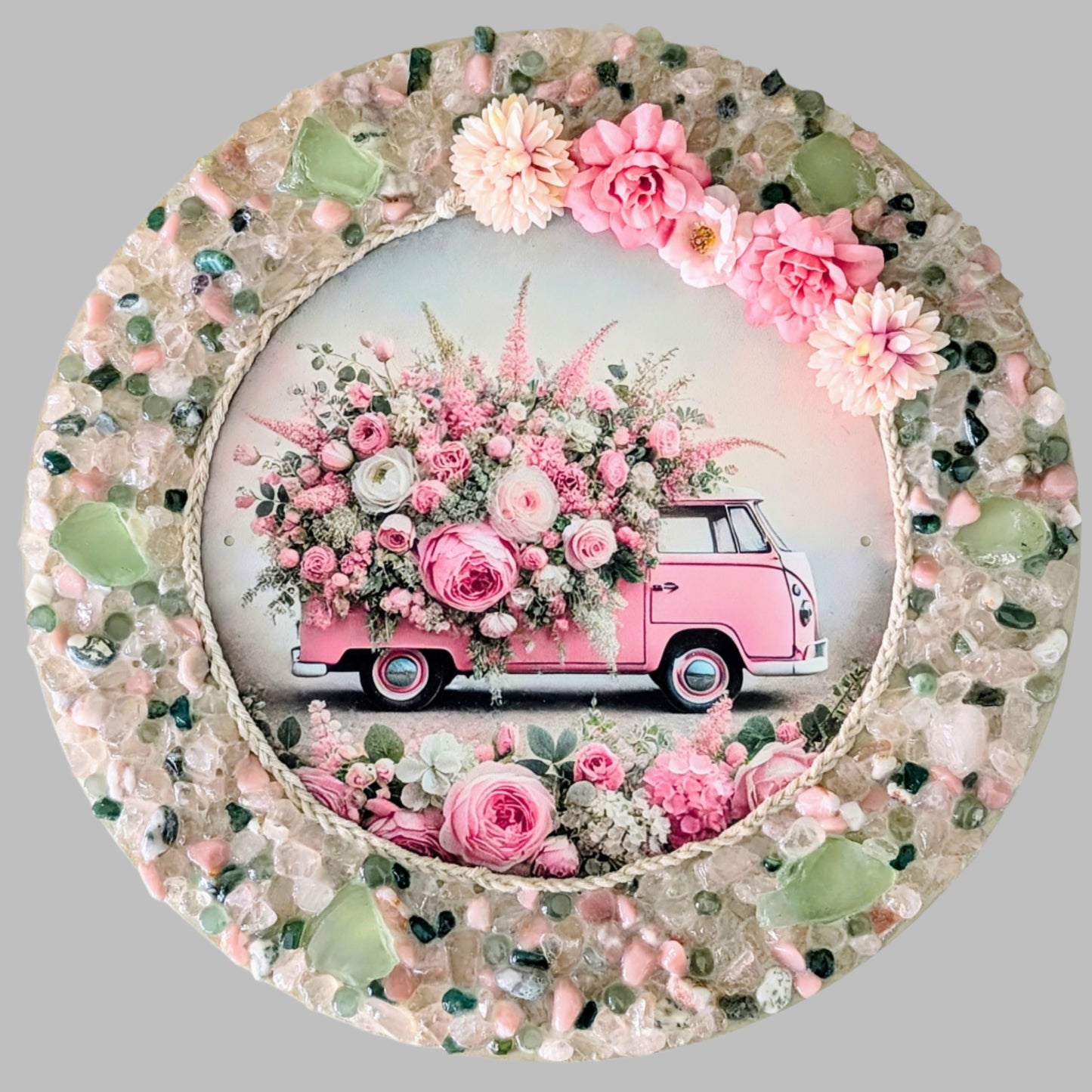 "The Blooming Kombi" is a handmade canvas featuring a print of a pink Kombi van adorned with flowers, framed with rope and surrounded by vibrant mint green, pink & clear stones & pebbles.
