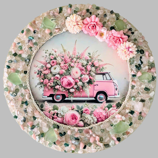 "The Blooming Kombi" is a handmade canvas featuring a print of a pink Kombi van adorned with flowers, framed with rope and surrounded by vibrant mint green, pink & clear stones & pebbles.