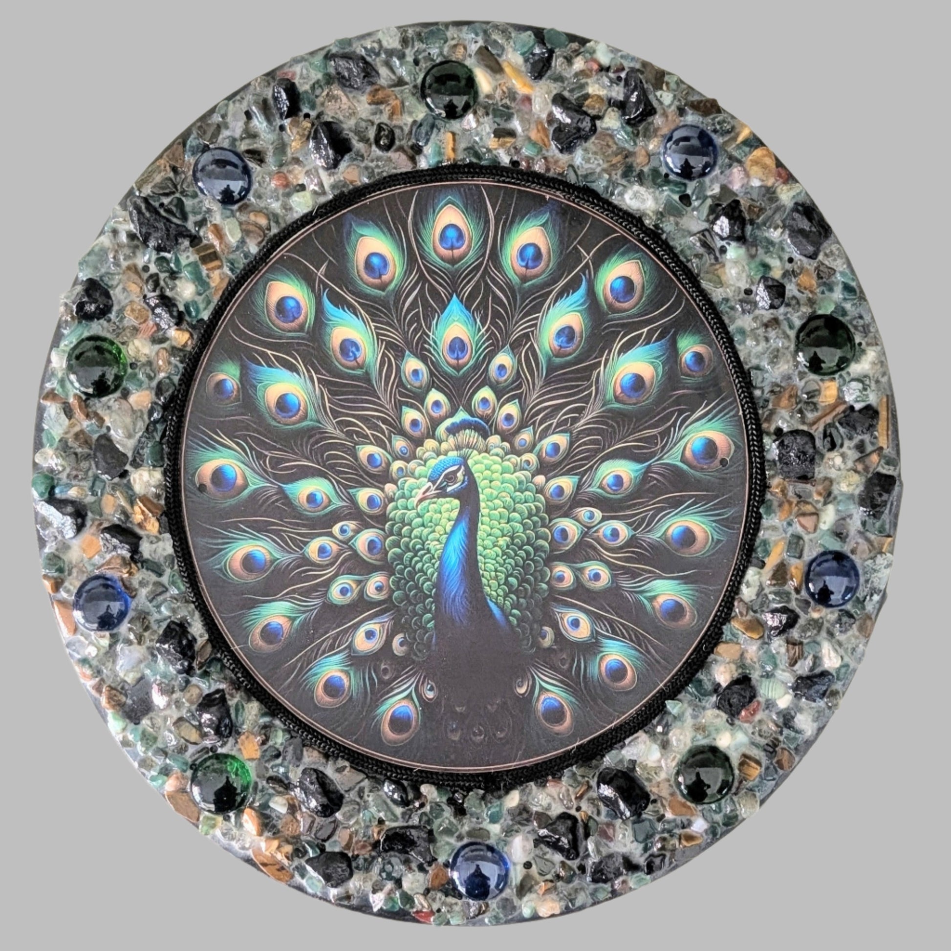 "A Lyrebird's Dance" is a handmade canvas featuring a print of a vibrant lyrebird framed by green, black, blue, and earthy stones, symbolising natural harmony.