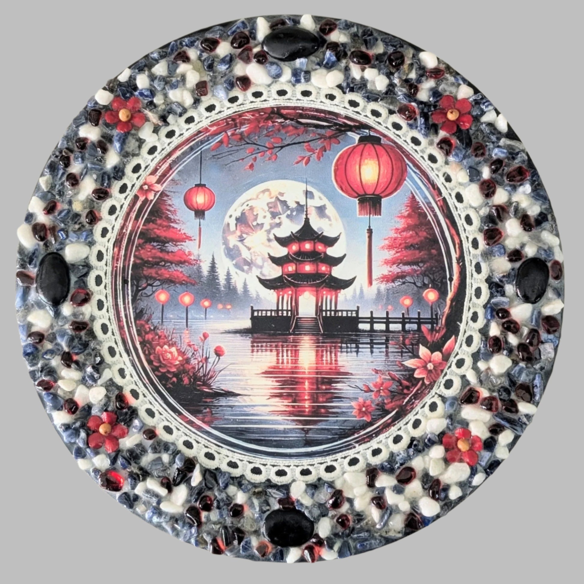 "Red Lantern Reflections" is a handmade canvas with a print of a Japanese teahouse, red lanterns, and serene water, decorated with vibrant red, blue and white stones and flowers.