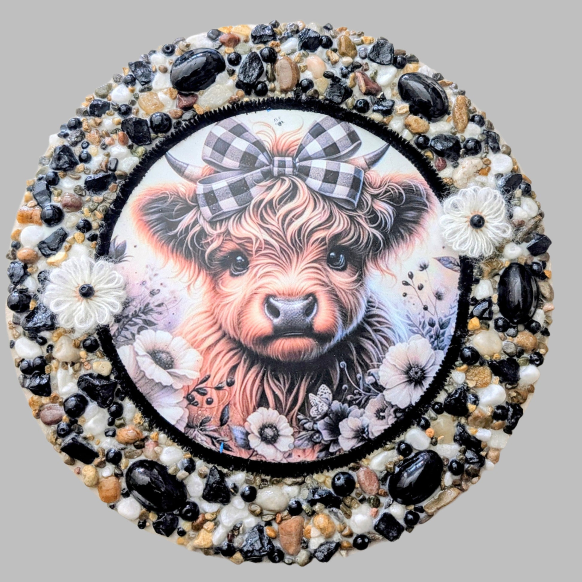 "The Tartan Heifer" is a handmade canvas featuring a print of a tartan-adorned cow decorated with white flowers, shiny stones, and earthy accents.