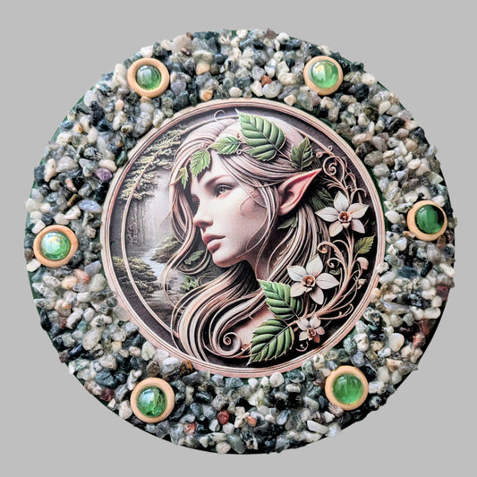 "Elf’s Sanctuary" is a handmade canvas featuring a print of an elf's face surrounded by green leaves, decorated with wooden rings and earthy stones, evoking woodland magic.