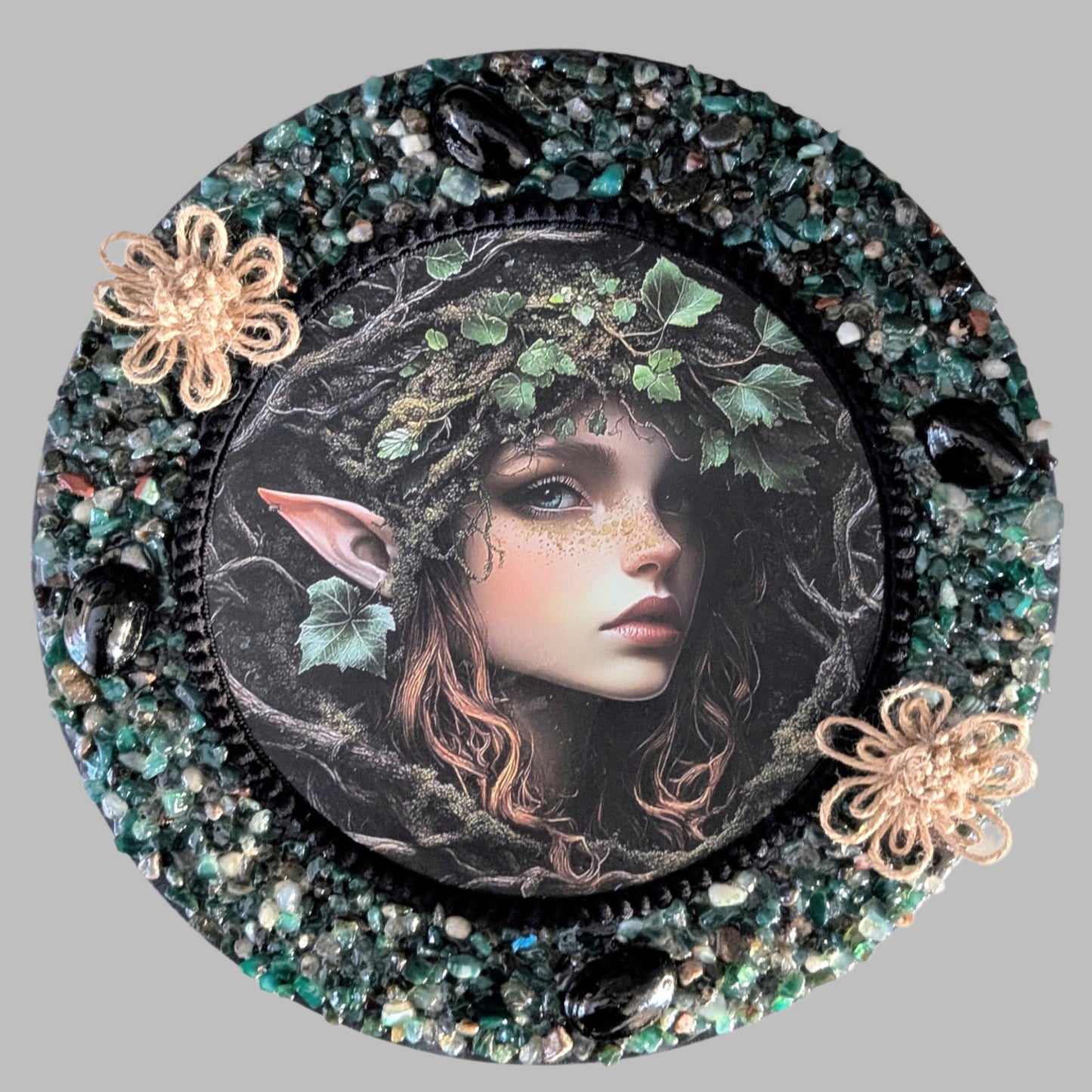 "Pixie’s Vines" is a handmade canvas featuring a print of a magical pixie surrounded by twisting vines, decorated with bold and earthy pebbles, evoking nature’s magic.