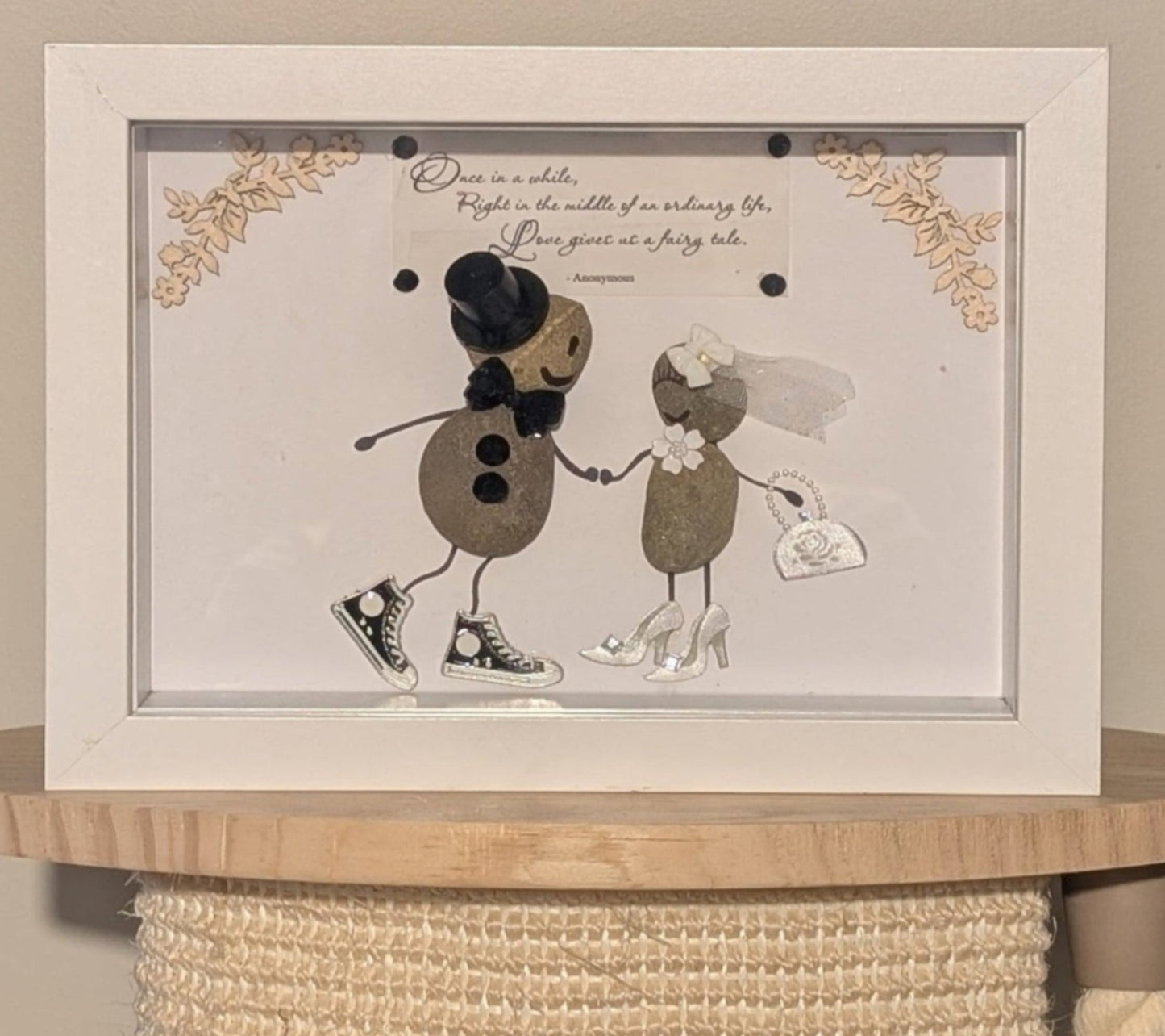 "Framed pebble art capturing a couple's special day with playful, modern details and rustic wooden edges, symbolising love and individuality."