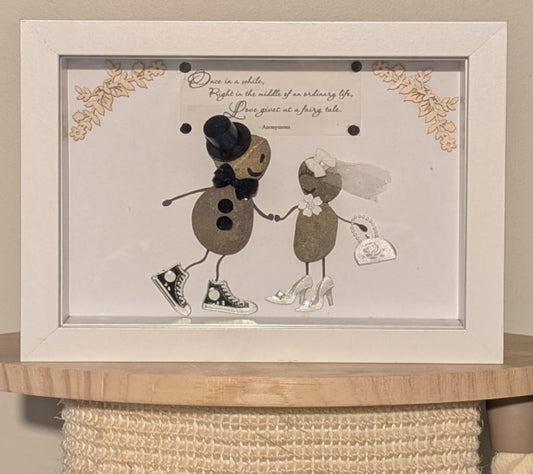 "Framed pebble art capturing a couple's special day with playful, modern details and rustic wooden edges, symbolising love and individuality."