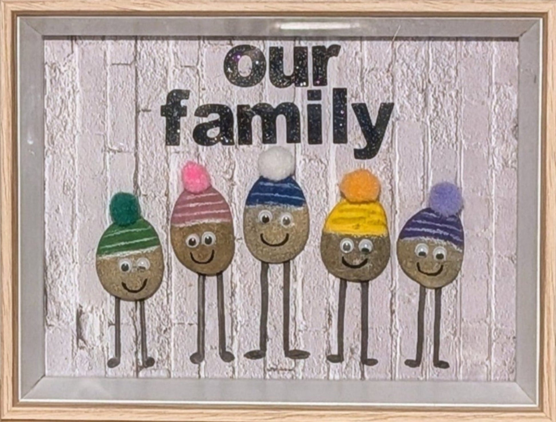 Framed pebble art of a stone family with colourful beanies, symbolizing strength, togetherness, and warmth, capturing the playful spirit of family bonds.