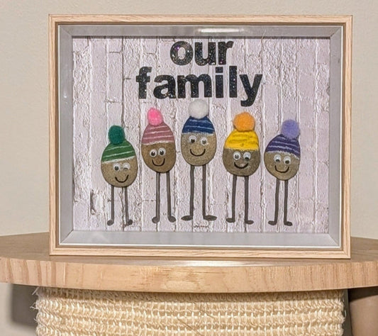 Framed pebble art of a stone family with colourful beanies, symbolizing strength, togetherness, and warmth, capturing the playful spirit of family bonds.