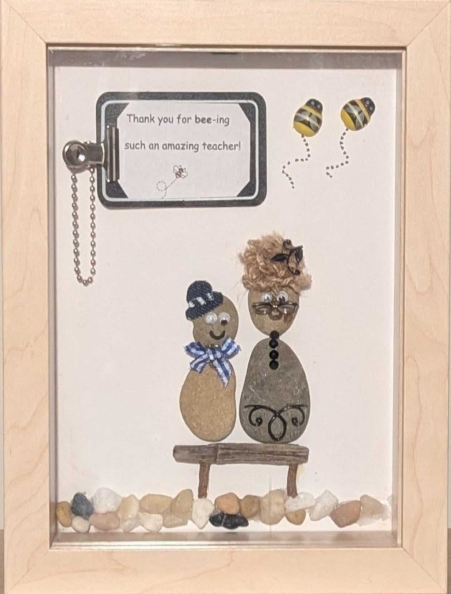 Framed pebble art of a teacher and student in a classroom, with buzzing bees and a clipboard, symbolising the joy of learning and the energy of education.
