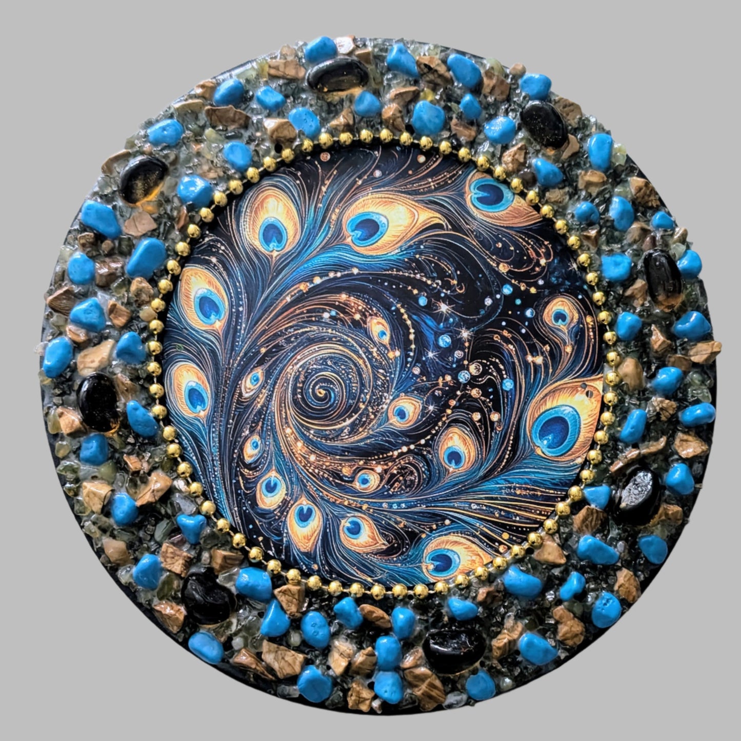Vibrant blue and gold stones and pebbles on a round canvas capturing the beauty and energy of a peacock's plume. 
